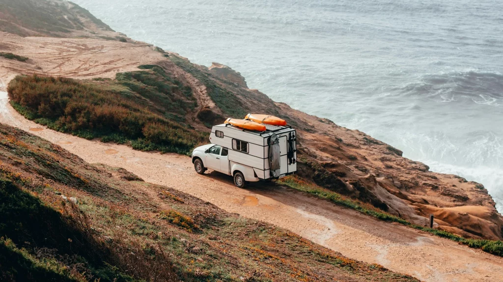 Imagen de una caravana pasando por un camino de tierra cerca del mar